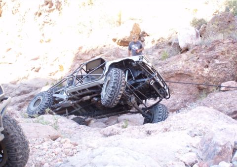 1986 Toyota Hilux - An off-road buggy with a custom roll cage is stuck on rocky terrain, with another vehicle partially visible in the foreground.