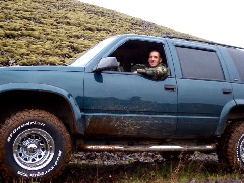1996 Ford Bronco - Man driving a teal SUV off-road, with mud splattered on the vehicle's side.