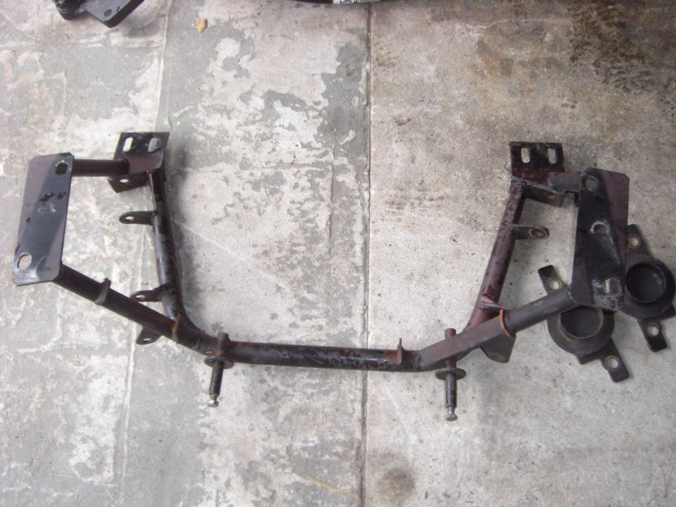 Rusty steel front crossmember with brackets and studs lying on a concrete floor