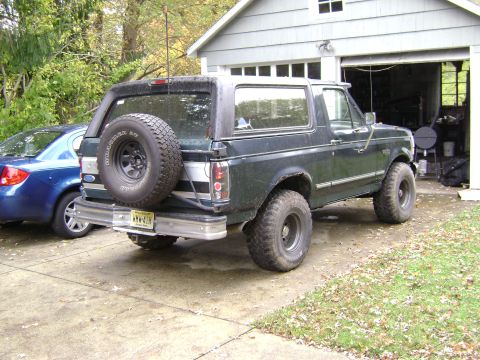 1994 Ford Bronco - This dark green Ford Bronco, likely from the early to mid-1990s, is parked in a driveway next to a blue sedan.