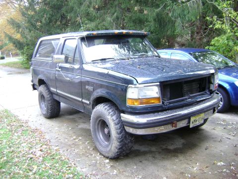 1994 Ford Bronco - This 1994 Ford Bronco features aftermarket wheels and a sun visor, parked next to another vehicle.