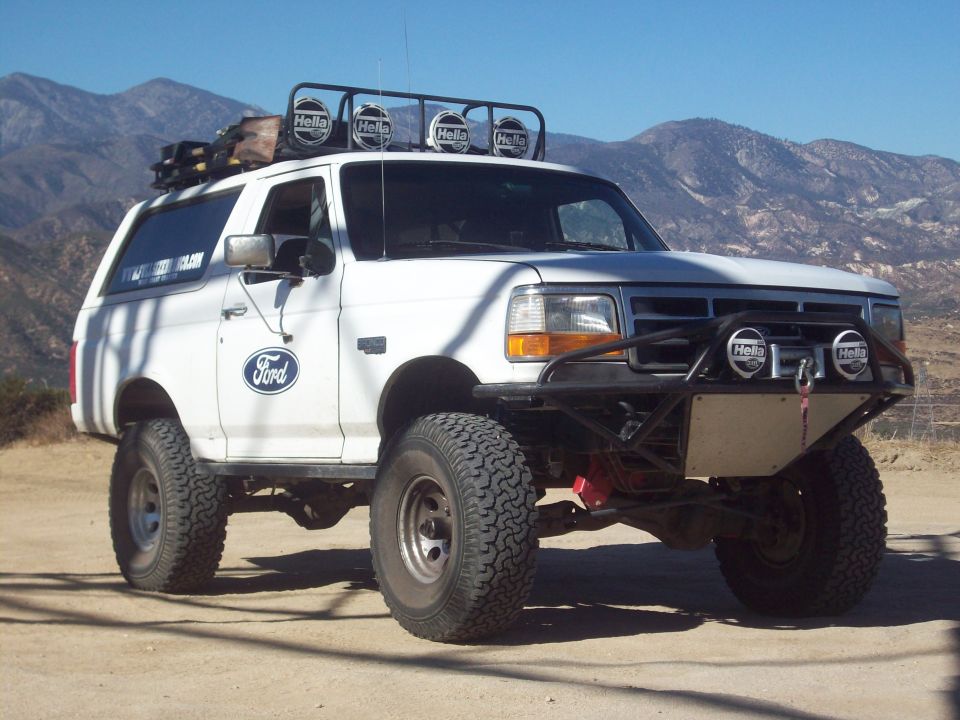 White lifted Ford Bronco with roof lights and front winch bumper on a dirt trail