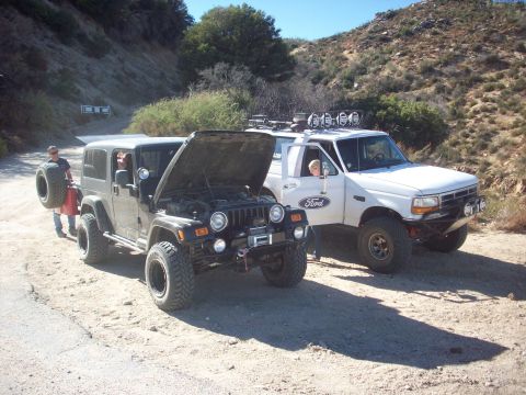 1995 Ford Bronco - A white 1995 Ford Bronco is parked on a dirt road next to a Jeep, with off-road lights mounted on the roof.