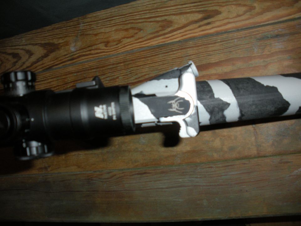 Rifle scope with black and white camouflage pattern on barrel, mounted on wooden surface
