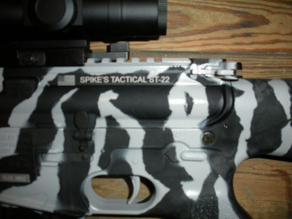 AR-15 rifle with black and white zebra-like camouflage paint, scope mounted on top, and 'SPIKE'S TACTICAL ST-22' marking