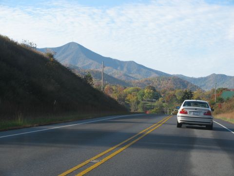 1985 Ford LTD Crown Victoria - A white sedan travels down a highway with a mountain range visible in the distance.