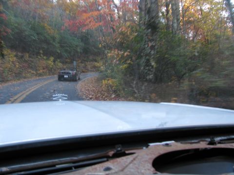 1985 Ford LTD Crown Victoria - A black convertible drives ahead on a winding road surrounded by colorful autumn foliage.