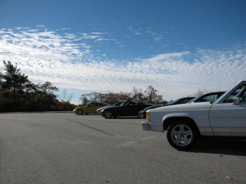 1985 Ford LTD Crown Victoria - A white 1985 Ford Crown Victoria LTD is seen from the front quarter angle, parked alongside other vehicles under a cloudy blue sky.