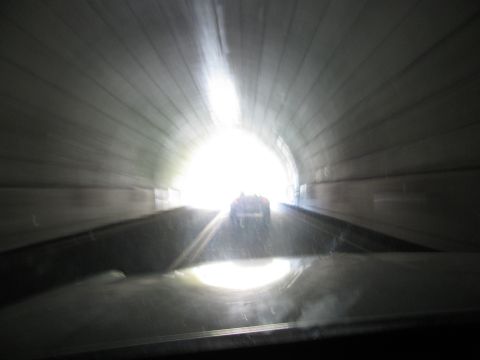 1985 Ford LTD Crown Victoria - A car travels through a tunnel, its rear lights barely visible as it heads towards the bright exit.
