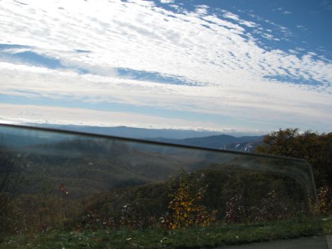 1985 Ford LTD Crown Victoria - A scenic view of rolling hills and a cloudy sky, seen through a car's side window.