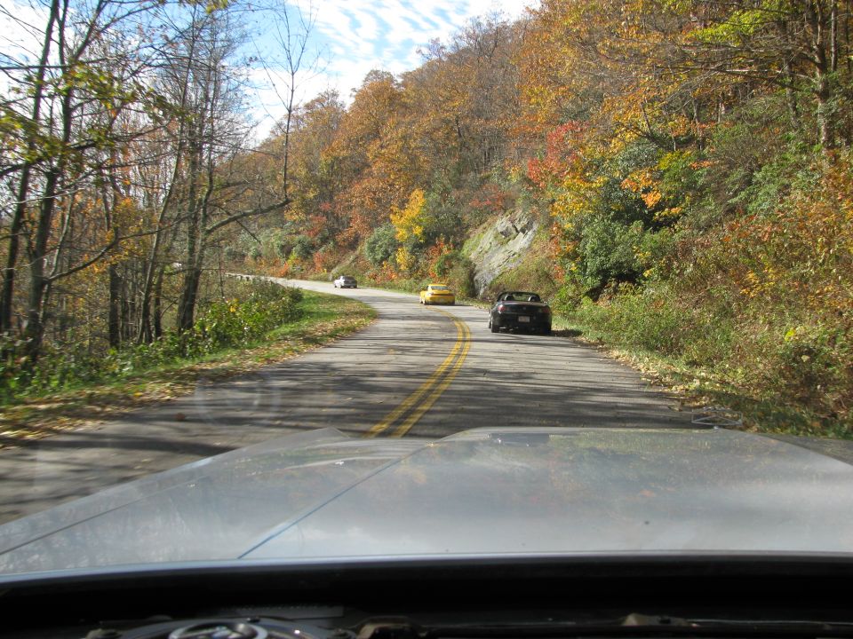 Dark convertible parked on a winding road with autumn foliage