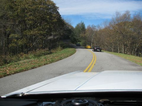 1985 Ford LTD Crown Victoria - Three cars are visible on a winding road through a wooded area on a sunny day.