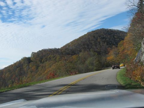 1985 Ford LTD Crown Victoria - Two cars drive along a scenic mountain road during the fall season.