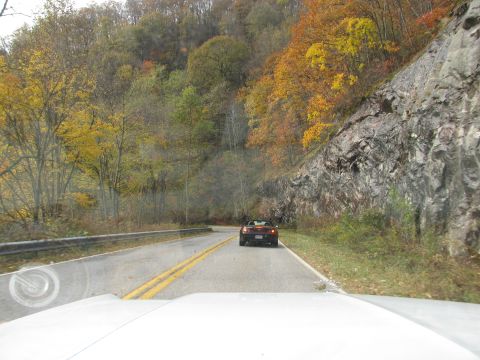 1985 Ford LTD Crown Victoria - A red convertible navigates a scenic road during the fall season, with trees displaying vibrant colors.