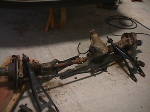 1996 Ford Bronco - A disassembled front axle assembly rests on supports, with visible suspension and braking parts.