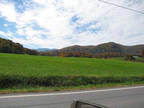1985 Ford LTD Crown Victoria - A scenic view of a rural landscape during the fall season with rolling hills and a vast green field.