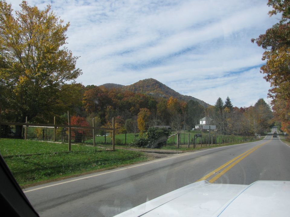 Driving down a two-lane road through a rural area with fall foliage and mountains in the distance