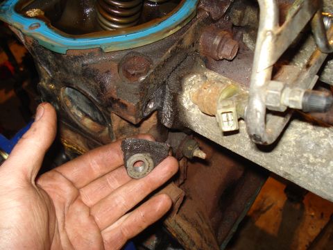 1991 Ford Bronco - A hand holds a damaged engine part against a greasy engine block, with springs and a gasket visible.