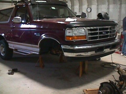1996 Ford Bronco - The front of a maroon Ford Bronco is raised on jack stands inside a garage, possibly for maintenance.