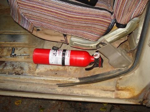 1967 Ford F-250 - A red fire extinguisher and a socket wrench lie on the rusty floor of a vehicle's interior.