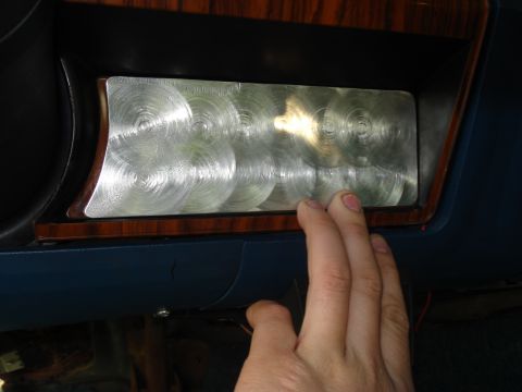 1984 Ford Bronco - A hand is shown touching a custom brushed aluminum panel installed in a vehicle's dashboard, surrounded by wood trim.