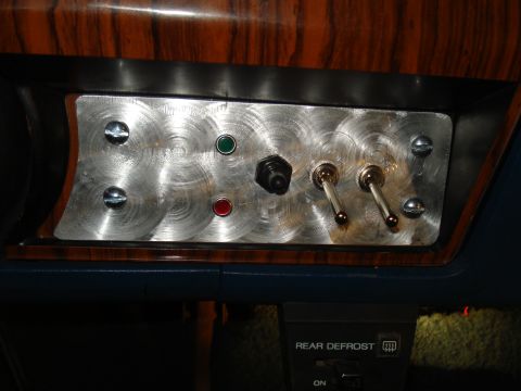 1984 Ford Bronco - Custom dashboard panel features toggle switches, indicator lights, and a rotary knob, set against wood grain trim.