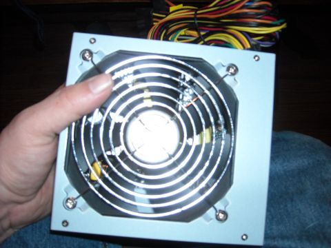 1979 Ford F-150 - A computer power supply unit is held in hand, with a fan visible on top and a bundle of colorful wires in the background.