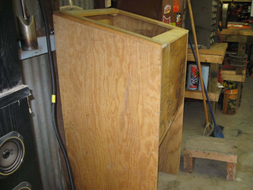Wooden cabinet with an open top in a workshop, next to speakers and tools