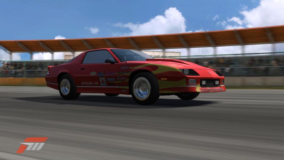 Red sports car with yellow flame decals on a race track, blurred background with spectators