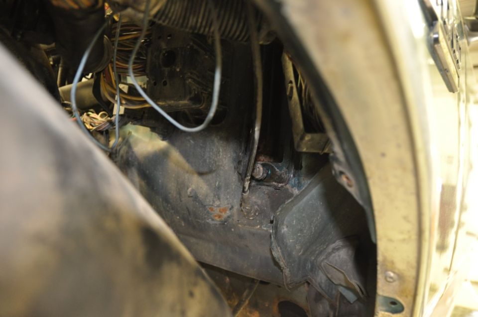 Stripped front fender well of a truck showing rusty frame, loose wiring and splash shield