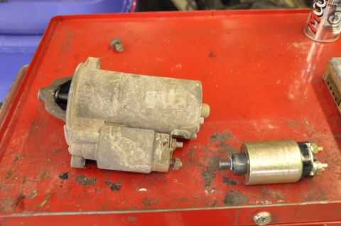 1996 Ford Bronco - Two automotive starter components are shown on a red metal surface, possibly a mechanic's workbench.