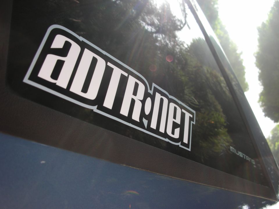Blue car side window with ADTR.net sticker and faint MUSTANG badge
