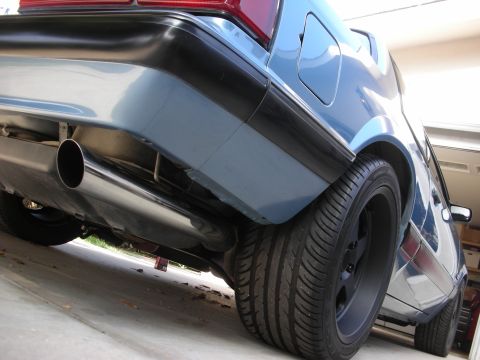 1990 Ford Mustang - The rear bumper and exhaust system of a blue car are visible from a low angle.