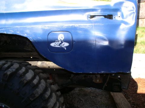 1979 Ford Bronco - A blue vehicle's rear quarter panel shows damage and a custom Ford fuel door with a pin-up graphic.