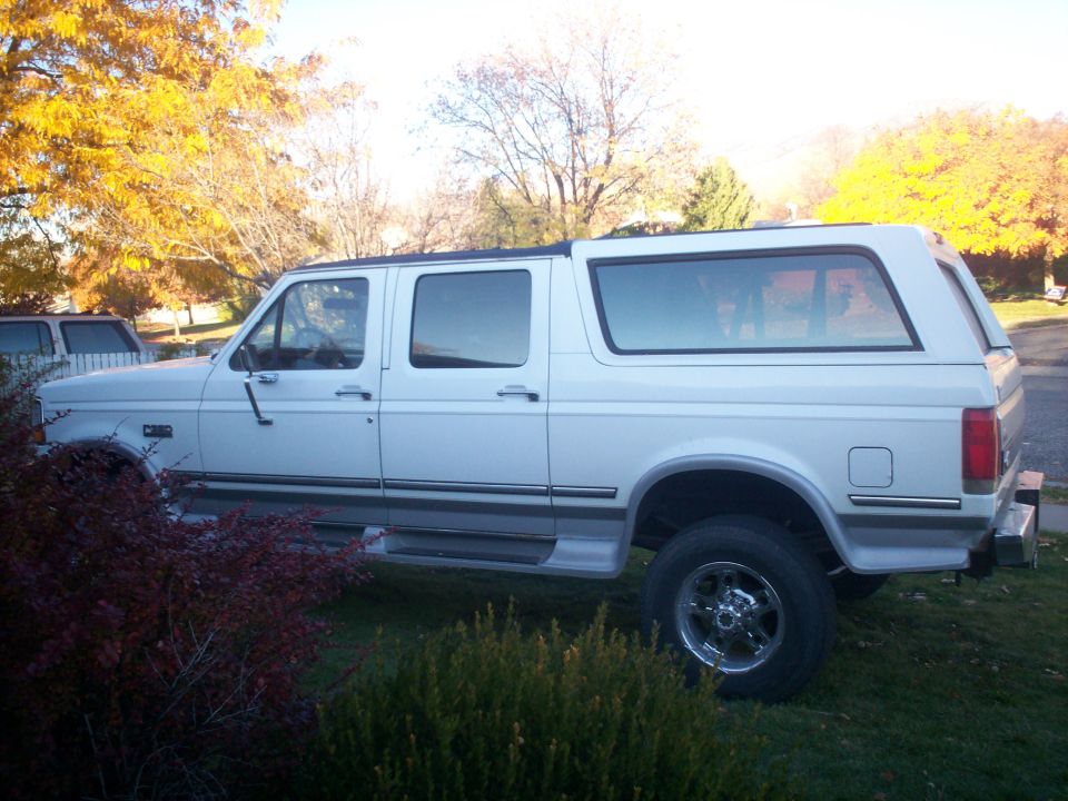 White extended cab pickup truck with a camper shell, seen from the side