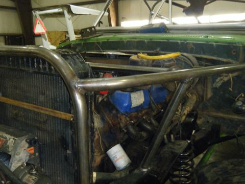 1978 Ford Bronco - Custom roll cage obscures the engine bay of a green vehicle, showing an oil filter and various engine parts.