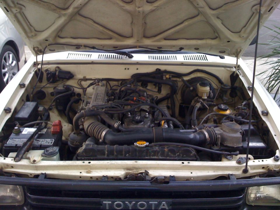 1989 Toyota Pickup/SR5 engine bay with hood open. Shows engine, battery, radiator, and hoses