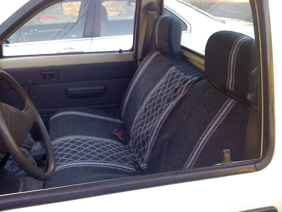 Pickup truck interior with patterned seats and a steering wheel. Another vehicle is visible through the window