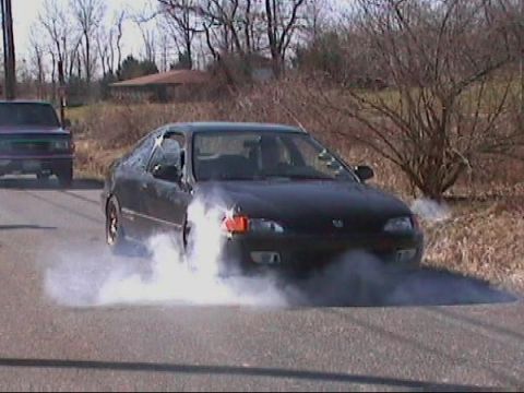 1982 Oldsmobile Cutlass - A black coupe performs a burnout, kicking up smoke, with a purple truck visible in the background.