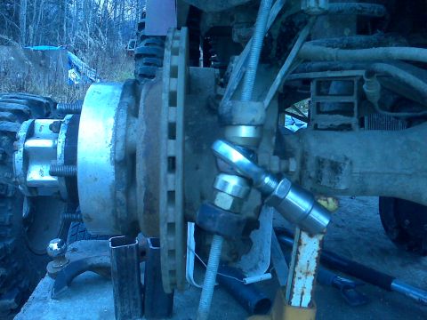1987 Suzuki Samurai - A close-up view of a vehicle's suspension and brake system, showing mechanical components and a tool in use.