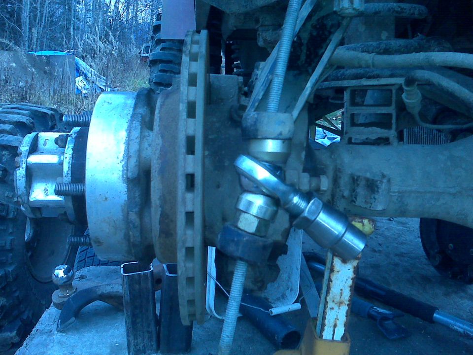 close-up of vehicle's front wheel hub, brake rotor, and suspension linkage with a wrench on a bolt