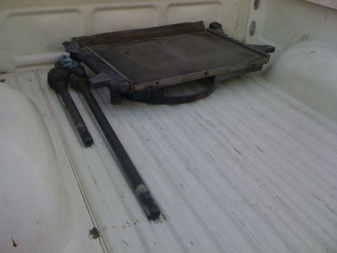 1989 Ford Bronco - Radiator and tie rods are stored in the bed of a white pickup truck.