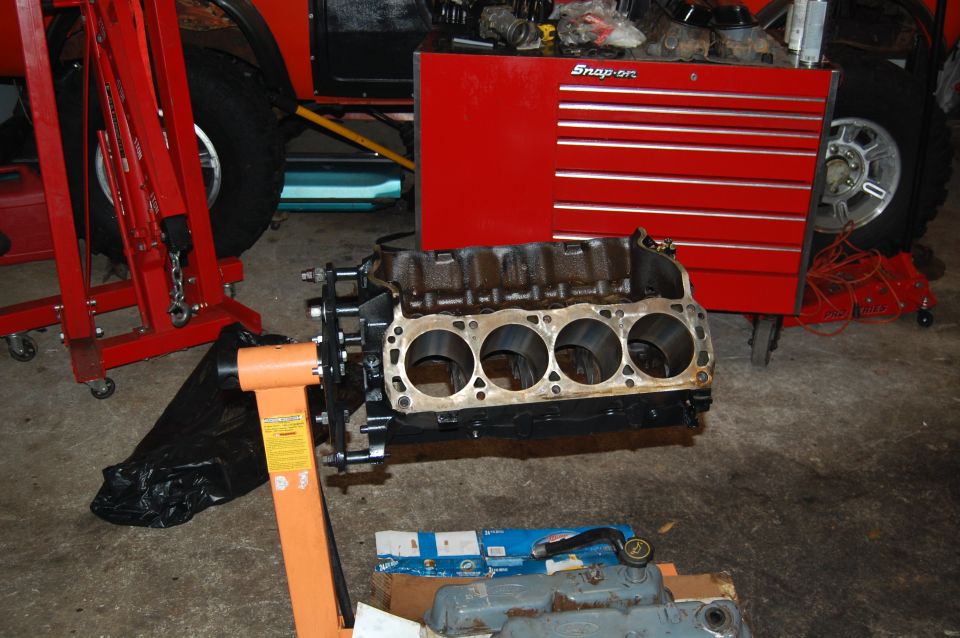 Engine block on an orange engine stand, with a red Snap-on tool chest and part of a red vehicle in the background