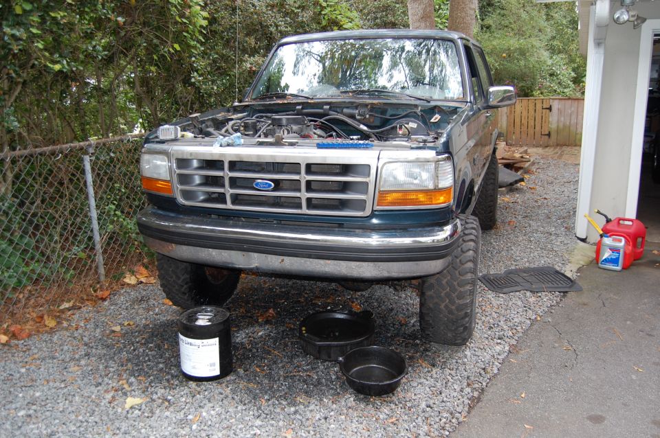 1994 Ford Bronco with hood open, parked on gravel with oil drain pans underneath