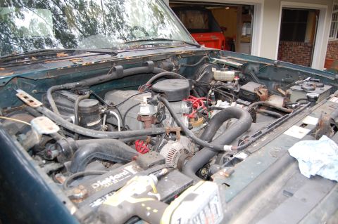 1994 Ford Bronco - The engine bay of a green vehicle is shown, with a red SUV parked in a garage in the background.