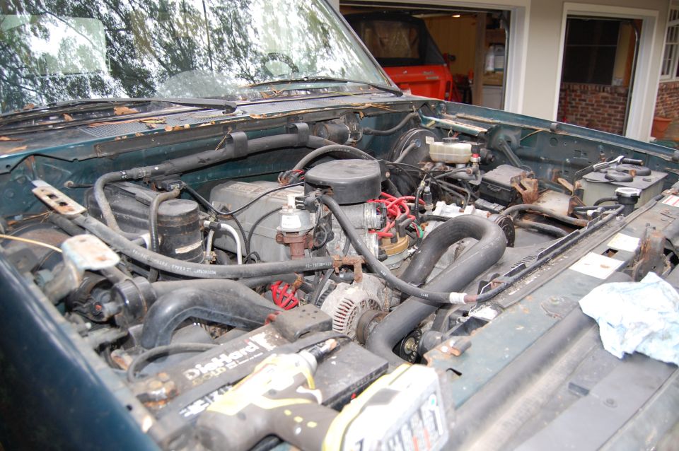 Engine bay of a green vehicle with a red SUV visible in the background