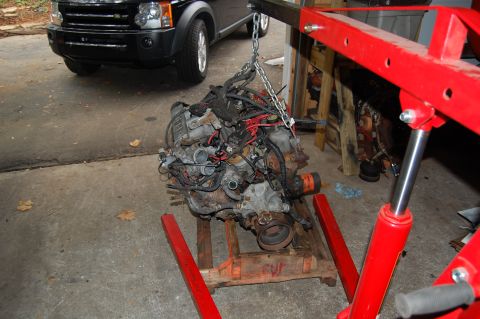 1994 Ford Bronco - An engine is being lifted by a red engine hoist in a garage setting.
