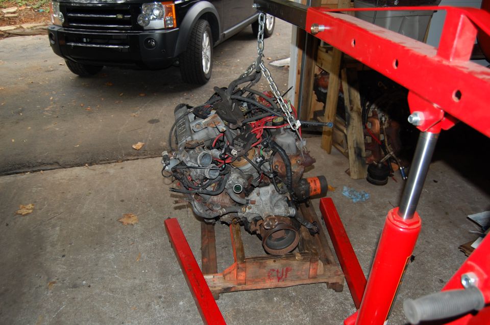 Engine assembly suspended by a red engine hoist over a wooden pallet