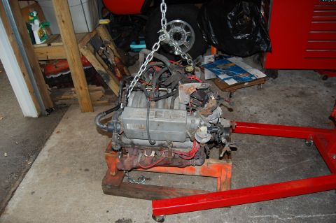 1994 Ford Bronco - An engine is suspended by chains and resting on an engine stand in a garage setting.