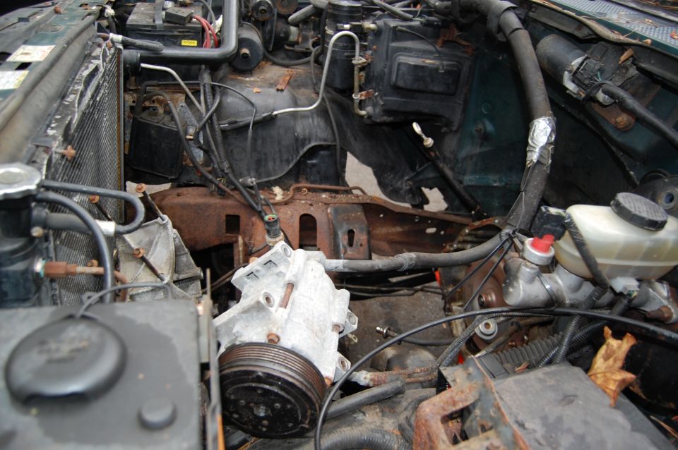 Engine bay with parts removed, showing the radiator, compressor, and brake fluid reservoir